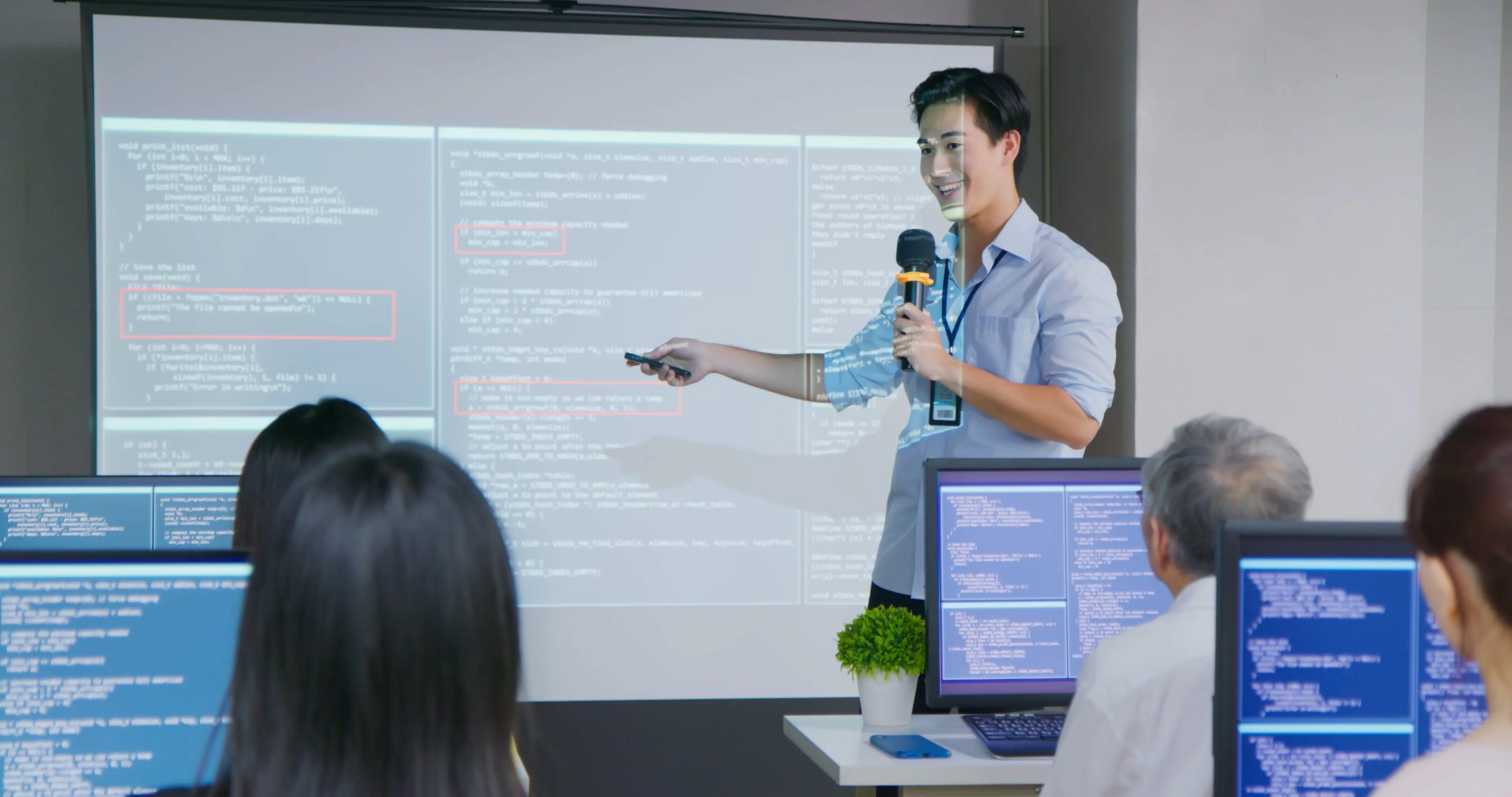 close up asian male teacher is speaking in adult education class with slides on computer screen - students sitting on chair using pc learning programming